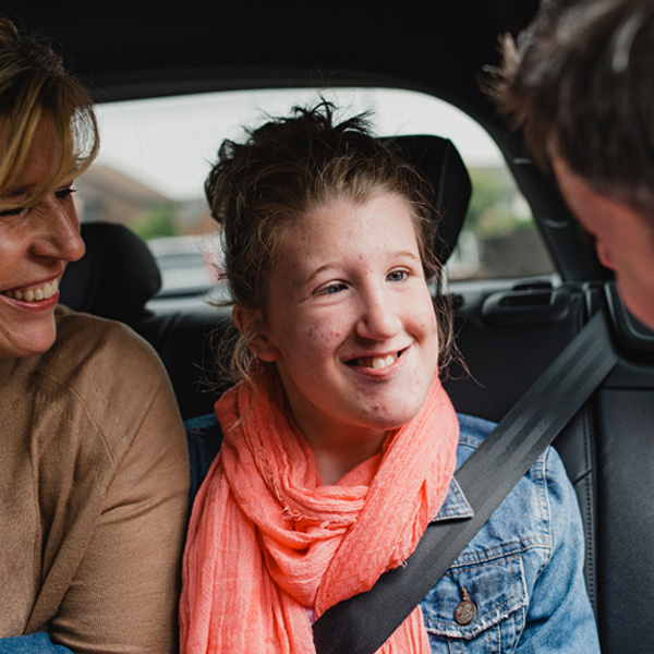 A young adult smiling in the car with her parents